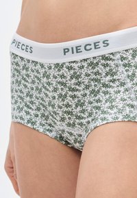 Žalias gėlių rašto kelnaitės su balta elastine juosta, kurioje matomas „PIECES“ logotipas. Pagamintos iš minkštos, tekstūruotos medžiagos, užtikrinančios komfortą.