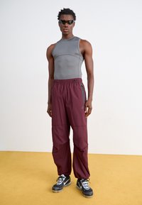 Haut gris ajusté sans manches associé à un pantalon maroon ample avec poches zippées, et des chaussures noires avec une semelle texturée.