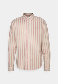 Camisa abotonada en beige con rayas verticales rojas. Presenta un cuello clásico, mangas largas y un pequeño detalle de logotipo en el pecho.