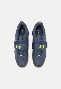 Dark blue athletic shoes with a textured upper, green accents, and a velcro strap. Features a rubber sole and perforated detailing.