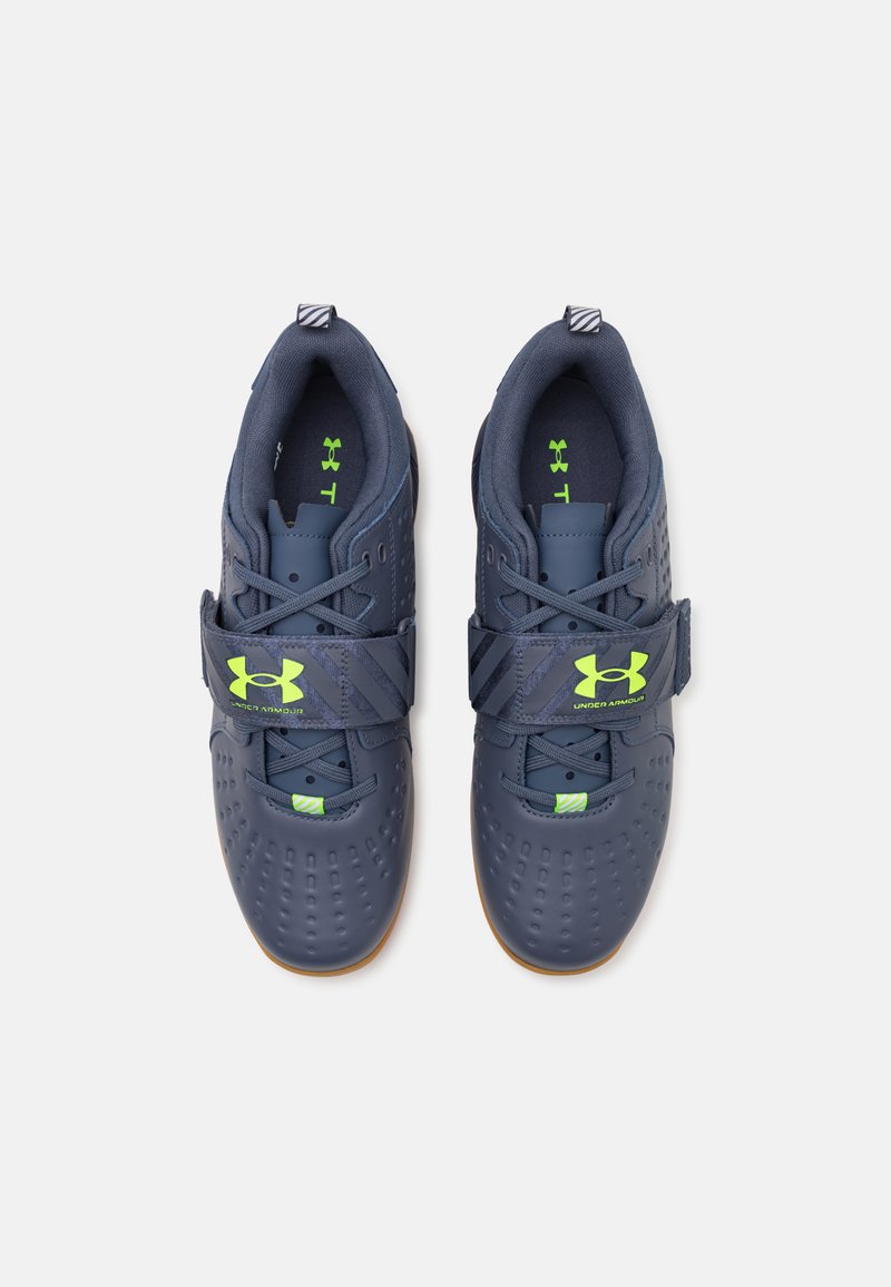 Dunkelblaue Sportschuhe mit einer strukturierten Oberseite, grünen Akzenten und einem Klettverschluss. Sie verfügen über eine Gummisohle und durchbrochene Details.