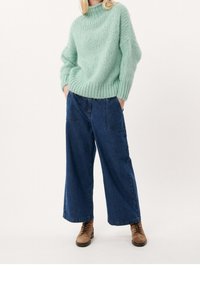 Mintgrön stickad tröja med hög hals och lös passform. Kombineras med mörkblå vida denimbyxor och bruna snörstövlar.