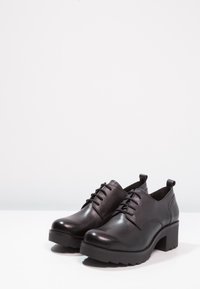 Svart läder snörskor med en kraftig klack, texturerad yta och dragflik bak. Har en något upphöjd tå och en stadig sula.