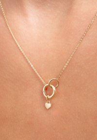 Goudkleurige ketting met in elkaar grijpende cirkelvormige schakels en een klein hartvormig hangertje. De ketting heeft een fijne textuur en een delicate uitstraling.