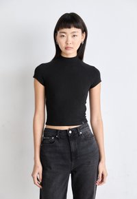 Musthave musternapärd musta lühikese varrukaga topp kõrge kaelusega; istuv disain. Koos kõrge vöökohtaga kitsaste mustade teksadega, millel on peened brändi detailid.