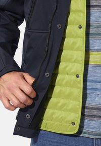 Navy outer jacket with a green quilted lining, featuring a zipper and snap buttons. Hand gripping the zipper, worn over a striped shirt.