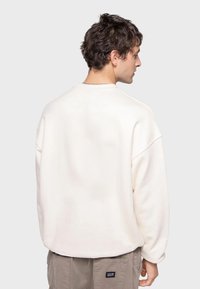 Witte sweatshirt met een relaxte pasvorm, verlaagde schouders en een geribbelde halslijn. De stof lijkt zacht met minimale detailing.