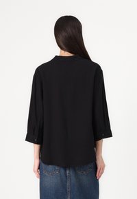 Black, lightweight blouse with a collar and three-quarter sleeves, featuring button accents. Smooth texture with a classic cut.