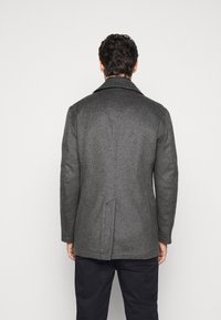 Grå uldfrakke med skråkrave, rygventilation og skræddersyet pasform. Glat tekstur, knælængde og minimalistisk design.