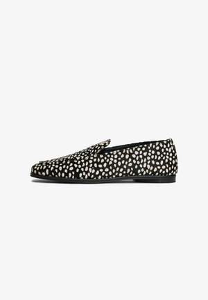 Black slip-on loafer with white irregular polka dots and flat sole, viewed from the side on a white background.