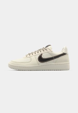 Beige leren sneakers met een witte rubberen zool, voorzien van een donkerbruine swoosh, gestikte details en grijze veters.