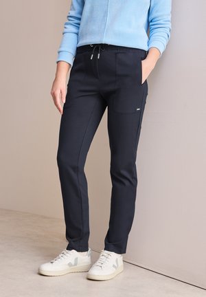 Námořnické modré džínové kalhoty s elastickým pasem na šňůrku, předními kapsami a slim fit, v kombinaci s bílými teniskami s světle šedými akcenty.