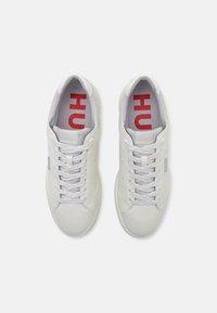 Witte sneakers met een gladde leren afwerking, ronde neus, vetersluiting en contrasterende rode en grijze inlegzool branding.
