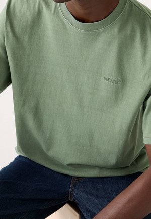 Light green cotton t-shirt with a crew neckline and short sleeves, featuring an embossed Levi's logo on the chest. Worn with dark jeans.