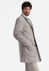 Abrigo de lana gris claro con un cuello muesca, dos bolsillos frontales y un ajuste relajado. La tela presenta una sutil textura con patrón.