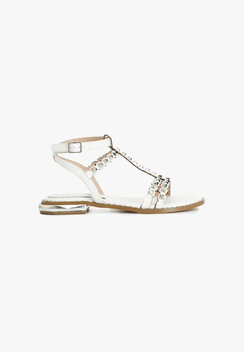 White flat sandals with a T-strap design, featuring silver stud accents, a small angled heel, and a smooth leather finish.