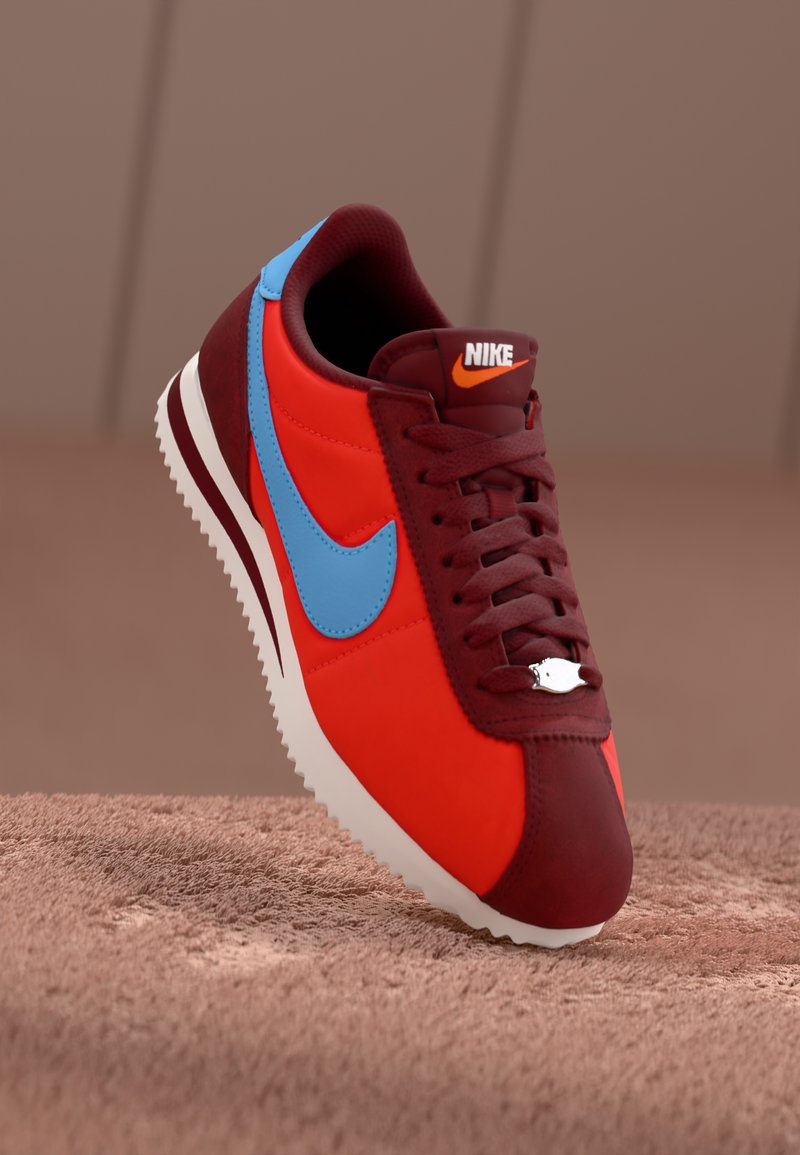 Tenisky Nike v červené a modré barevné kombinaci, vyrobené z kůže a syntetických materiálů, s texturovanými tkaničkami a bílou gumovou podrážkou s trakčním vzorem.
