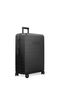 Valise rigide noire avec une texture nervurée, fermeture éclair, poignée extensible et quatre roues pour une mobilité facile.