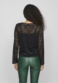 Black lace long-sleeve top with floral patterns and sheer sections, paired with green faux leather pants featuring a fitted design.