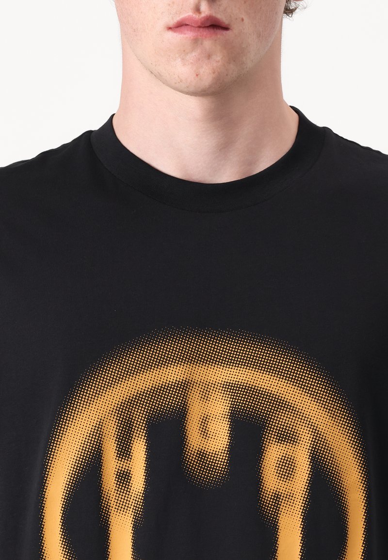 Schwarzes Baumwoll-T-Shirt mit großem gelbem Grafikdruck in gepunktetem Muster, zentriert auf der Brust, mit Rundhalsausschnitt.