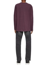 Langärmliges lila Shirt mit Rundhalsausschnitt, kombiniert mit dunkelgrauen Jeans und schwarzen Sneakern. Einfaches Design, entspannte Passform.