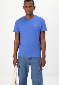Blå kortermet t-skjorte med rund hals og et lite logo-design i kontrasterende farger; kombinert med lyseblå cargo-jeans.