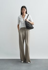 Κρεμ ριμπ πουκάμισο πόλο με κορδόνια μπροστά, συνδυασμένο με φαρδιά μπεζ παντελόνια με ζώνη. Το μοντέλο κρατάει μια υφασμάτινη μαύρη τσάντα.