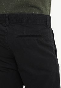 Svarta bomullsbukser med en slät yta, utrustade med en sidoficka och en bakficka med en horisontell slitsdesign.