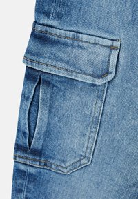 Close-up van blauwe denimstof met een overslagzak en stiksel details op een kledingstuk, waarschijnlijk jeans of een spijkerjasje.