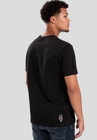 Camiseta de algodón negra de manga corta, con cuello redondo y un diseño gráfico colorido que presenta una pequeña figura de dibujos animados en la parte posterior.