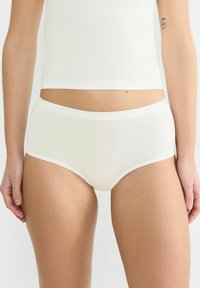 Naturale Baumwollslips in Off-White mit glatter Textur, elastischem Bund und kontrastierender weißer Borte entlang der Beine und Taille.