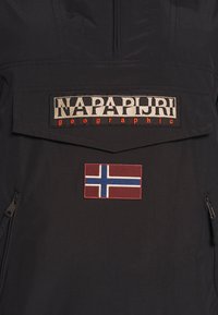 Veste noire devant avec un patch logo Napapijri Geographic au-dessus d'un patch drapeau norvégien et deux poches zippées sur les côtés.