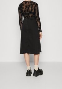 Svart denim midi kjol med rak skärning, har en sidofrak och är kombinerad med kraftiga svarta skor och ljusa strumpor.