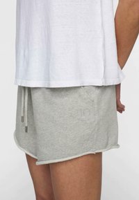 Pantalones cortos de algodón gris con cintura elástica ajustable, bolsillo lateral y bordes sin dobladillo. Los pantalones cortos presentan un número "10" bordado en el costado.