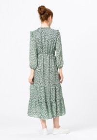 Robe midi verte à motif floral avec un ourlet à volants, des manches bouffantes et une taille élastique. Fabriquée en tissu léger et semi-transparent.