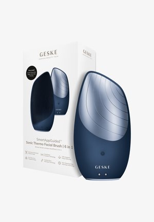 Mørkeblå GESKE Sonic termo-facial børste med strukturerede silikonebørster og buet design, vist ved siden af hvid produktemballage.