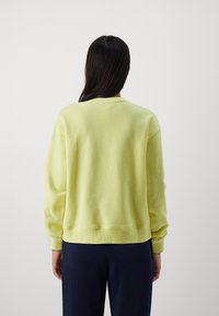 Lichtgele sweatshirt met een ronde hals, lange mouwen en geribde boorden. Textuurstof en een ontspannen pasvorm, gecombineerd met donkere broeken.