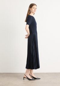 Knit navy dress with short sleeves and pleated skirt, combined with black slingback heels featuring a pointed toe and low heel.