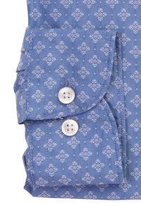 Manica di tessuto blu con un motivo floreale geometrico bianco, due bottoni bianchi e un dettaglio di polsino piegato.