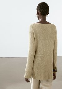 Maglione beige a costine con scollo ampio, maniche lunghe e una vestibilità leggermente oversize, abbinato a pantaloni chiari.
