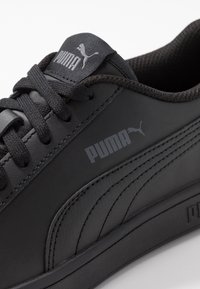 Černé kožené tenisky s texturovaným povrchem, které mají černé tkaničky, polstrovaný límec a bílé akcenty loga Puma po straně a na jazyku.