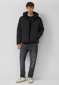 Czarna kurtka puchowa z kapturem, zapinana na zamek błyskawiczny, z bocznymi kieszeniami. Noszona na czarnej koszuli, w połączeniu z ciemnymi dżinsami i białymi trampkami.