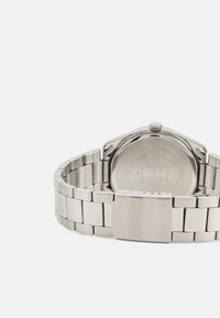 Montre-bracelet en acier inoxydable argenté avec un bracelet à maillons, un boîtier rond et une lunette lisse. Marquage gravé sur le fermoir et au dos du boîtier.