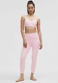 Light pink sports bra with thin straps and matching high-waisted leggings; smooth, stretchy fabric; form-fitting design; minimalist style.