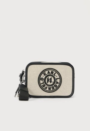 Sac bandoulière rectangulaire en toile beige avec bordure noire, logo circulaire Karl Lagerfeld sur le devant, et sangle noire ajustable avec ferrures argentées.