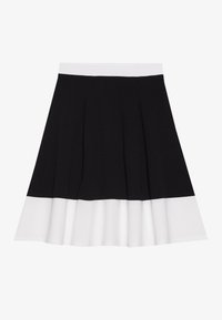 Jupe plissée noir et blanc avec une large ceinture blanche, présentant un haut noir uni et un ourlet blanc évasé. Texture de tissu lisse.