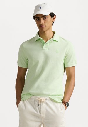 Lichtgroen poloshirt met korte mouwen en een kraag; klein geborduurd logo. Gecombineerd met beige gestreepte short. Witte pet en horloge.
