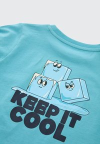 Tirkīza kokvilnas t-krekls ar apaļu kaklu, kurā attēloti trīs karikatūru ledus gabali un uzraksts "KEEP IT COOL" treknā melnā burtā.