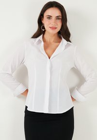 White button-up shirt with long sleeves, classic collar, and two chest pockets featuring pinstripe detailing. Smooth, lightweight fabric.