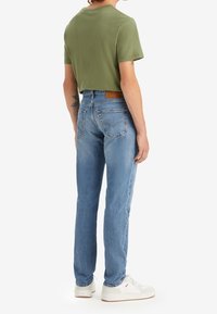 Grön t-shirt med korta ärmar kombinerad med ljusblå jeans med raka ben. Vita sneakers med en texturerad sula fulländar outfiten.